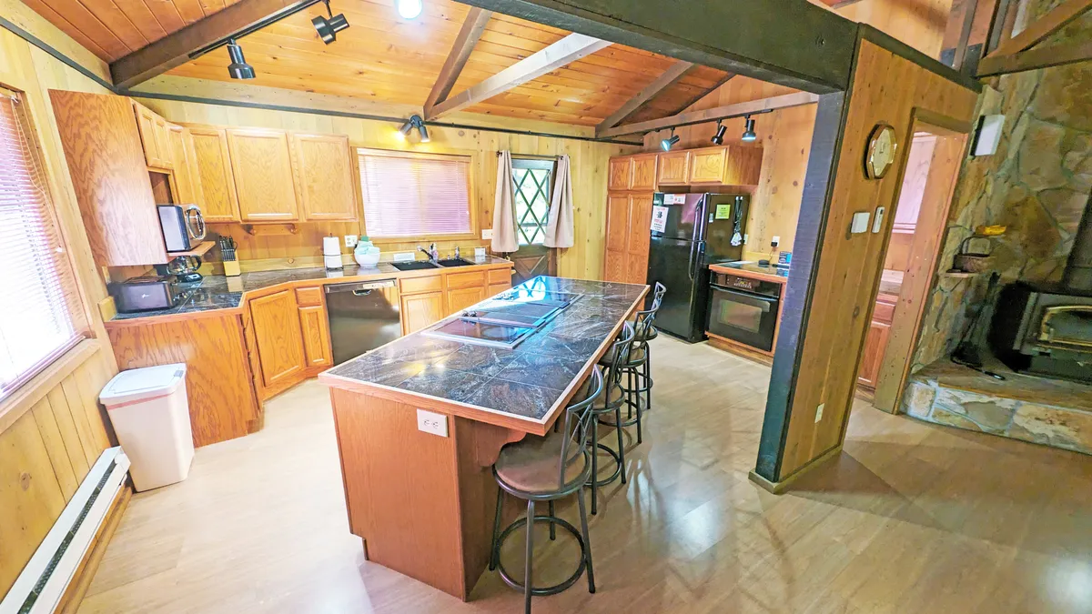 This image showcases a spacious kitchen island paired with warm wooden cabinetry and a cozy stone fireplace, presenting an inviting hub for morning coffees and group gatherings. The scene exudes warmth and social energy, with ample space for friends to congregate before setting out for the day.
