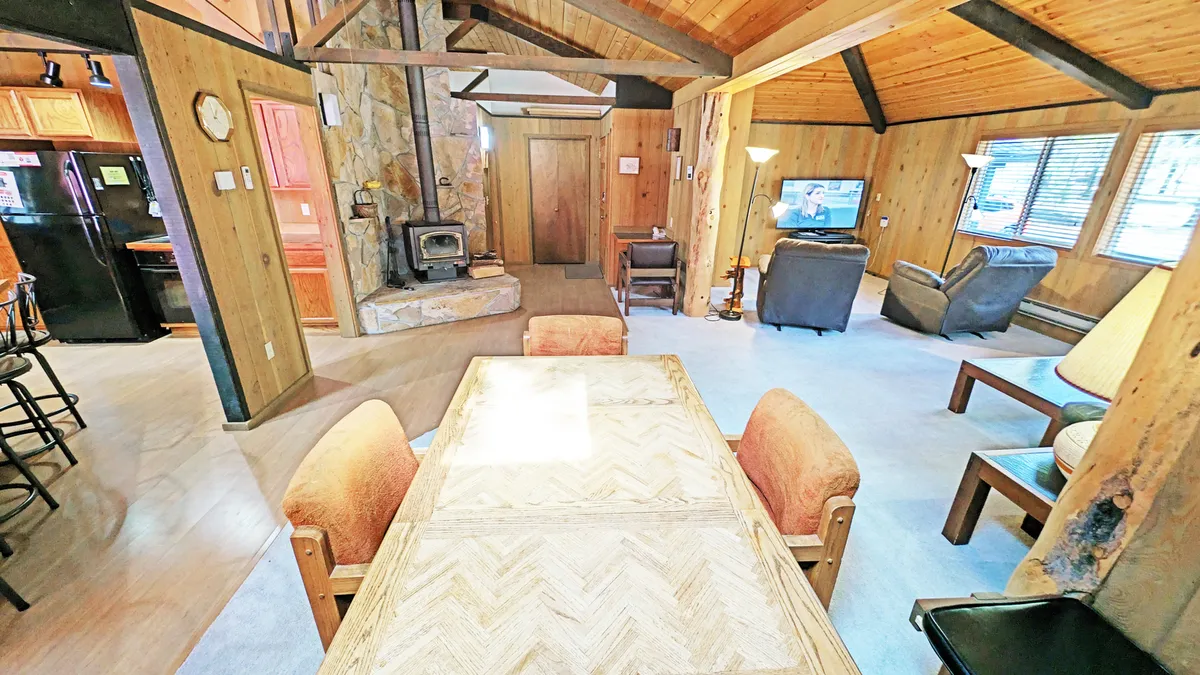 This image showcases an inviting open-concept living and dining area featuring a wood-burning stove, a spacious dining table, and comfortable seating. The view allows a glimpse of the space where guests can gather after a day of outdoor activities, unwind with meals, or relax by the fire.