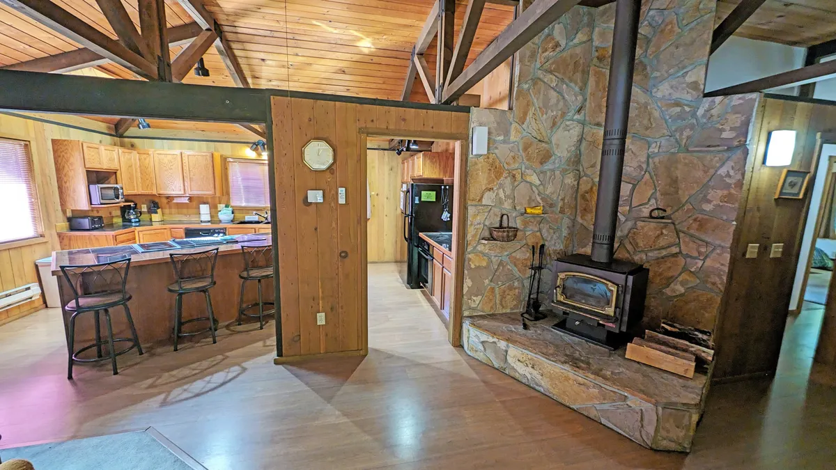 This image features a wood-burning stove, a kitchen island, bar stools, and a stone wall—creating a cozy, inviting space. The layout hints at comfortable evenings spent inside, ideal for families and pets winding down after a day of outdoor activities.