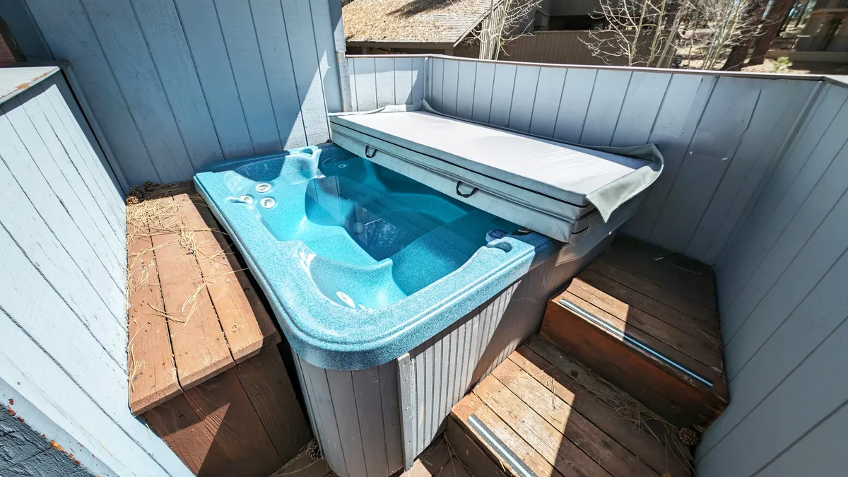 A serene view of a hot tub set on a wooden deck with privacy walls, inviting guests to enjoy a soak under the stars or during sunset. The scene exudes tranquility and relaxation in an outdoor environment.