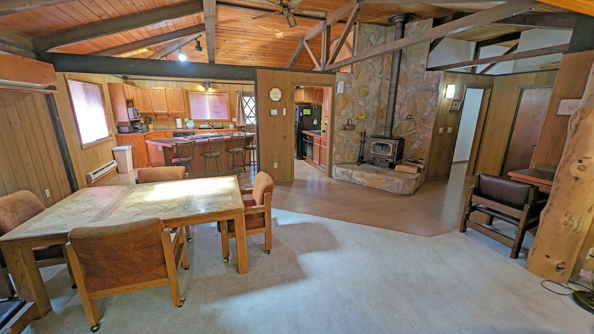 A spacious dining table set in an open kitchen area, with a stone fireplace nearby, offers a welcoming space for group meals and indoor socializing. The setting feels warm and inviting, ideal for group BBQs or shared dinners after a day out.