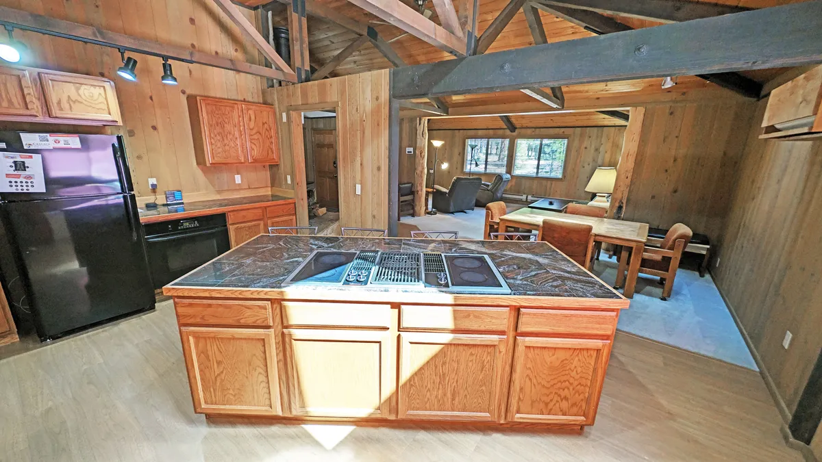 A well-lit, open-plan kitchen and dining area featuring a generous kitchen island, classic wooden cabinetry, an adjacent dining table, and a warm, welcoming atmosphere. The setup is ideal for both cooking and dining, allowing guests to seamlessly move between preparing meals and gathering at the table.